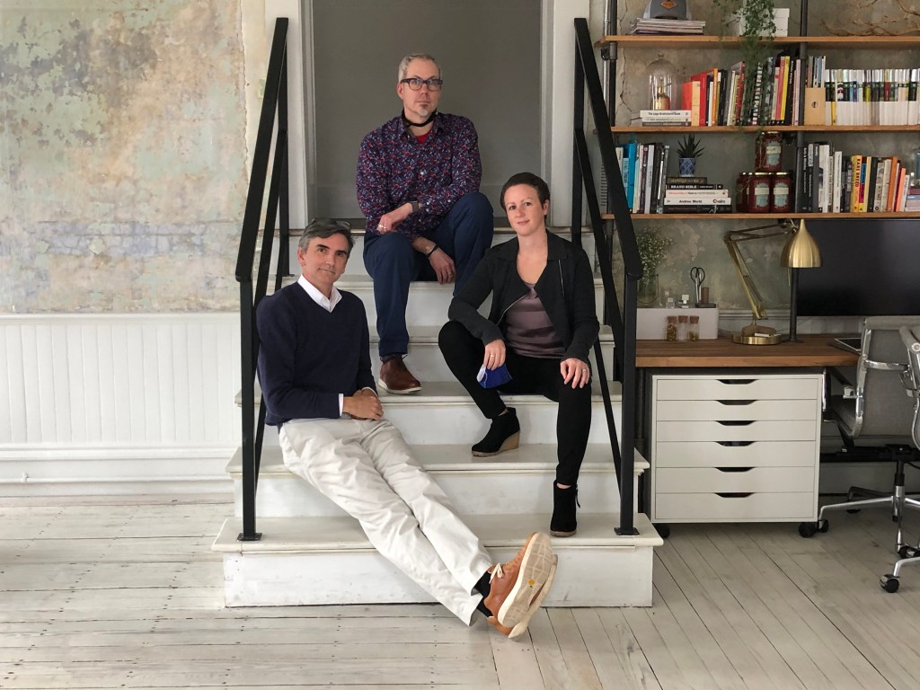 Ed, Jim, and Annie sit on a short flight of stairs in an office, in a triangular arrangement.